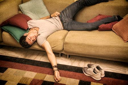 Photo of a young and handsome man resting in a strange position on the floor with a pillow under his head, maybe drunk or very tiredの写真素材