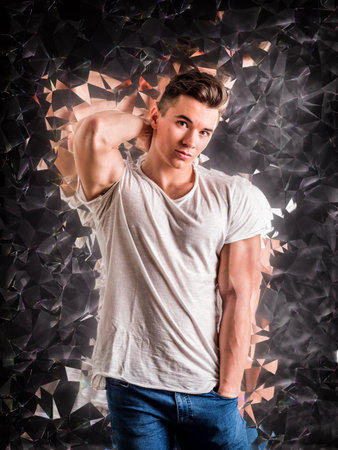 A young muscular man is posing for a picture, with specks and fragments of mirror reflecting him...