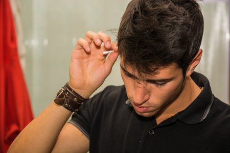 A young handsome man is cleaning his ears with a cotton stick. Photo of a man cleaning his ears with a cotton stickの写真素材