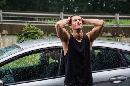 A man standing next to a car in the rain, sad because his vehicle broke downの写真素材