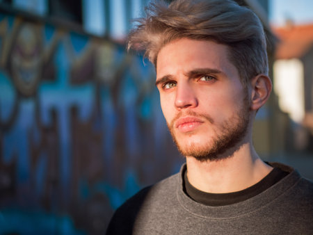 A man with blonde hair standing in front of a wall. Photo of a man with blonde hair standing in front of a wall, looking at cameraの写真素材