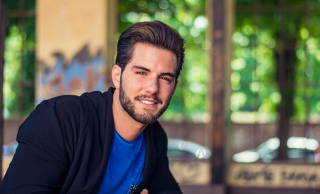 A man with a beard and a blue shirt. Photo of a bearded man wearing a blue shirt, looking at camera smiling. A joyful smiling young adult with a beard and casual clothing.の写真素材