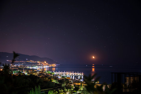 A night time view of a city and the Mediterranean Sea. Photo of the stunning night skyline of Diano Marina, a charming town nestled on the coast of Liguria, Italyの写真素材