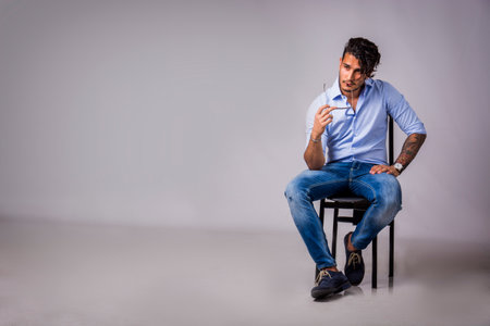 A young handsome man sitting on a chair holding his sunglasses. Photo of a man thinking while...