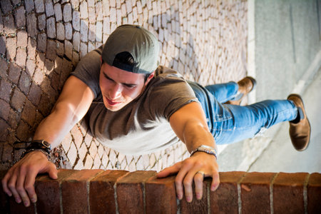 A young man hanging from a brick wall. Optical illusion shotの写真素材