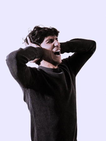 A young man with his hands on his ears, screaming and yelling in despair or frustrationの写真素材