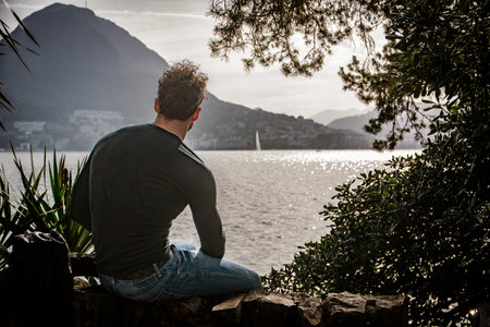 A man sitting on a rock looking out over a body of water in Lugano, Switzerlandの写真素材