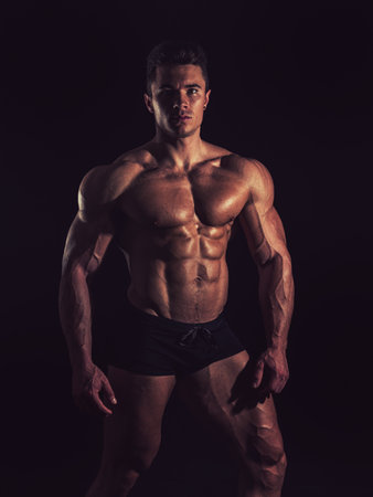A Strong Display of Masculinity: Flexing Muscles and Striking a Pose in Studio. A man posing for a picture while flexing his muscles in dramatic lights in studioの写真素材