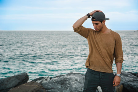 A young attractive man standing on top of a rocky beach next to the ocean or sea in autumn or winterの写真素材