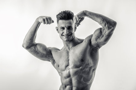 A bodybuilder man flexing his muscles in a black and white photo in studio, looking at camera smilingの写真素材