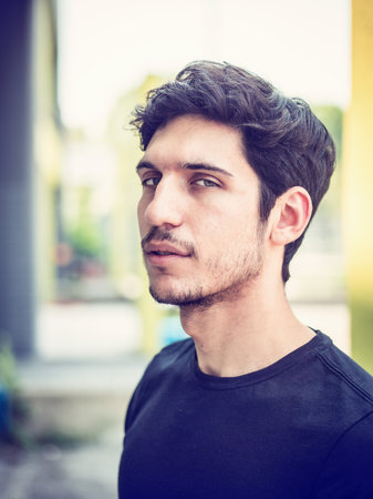 Head and shoulders shot of one handsome young man with green eyes in urban setting, looking at camera, wearing t-shirtの写真素材