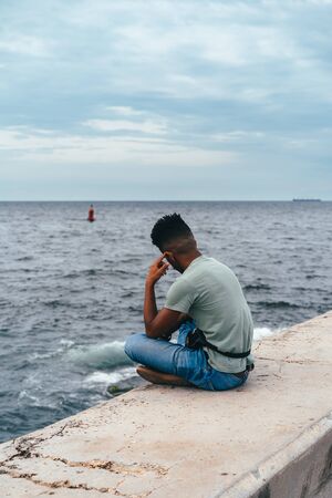 Latin guy in jeans sits on the promenade of the Caribbean in Havanaの写真素材