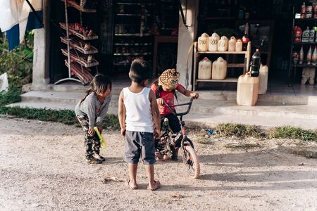 Three children from a poor neighborhood play on the street with a bicycle next to gas cansの写真素材