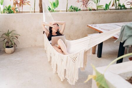 Girl with a laptop lies in a hammock on the terrace