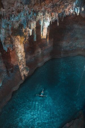 A girl in a swimsuit swims in a blue lake in a cenote cave on Yucatan in Mexico