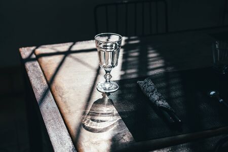 A glass goblet on a leg stands on a table among the shadows in the sunlightの写真素材