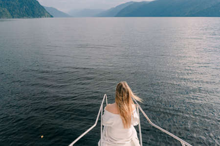A girl with hair fluttering in the wind stands on the bow of a boat floating on Lake Teletskoye...