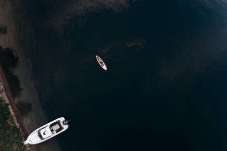 Aerial view from a drone to a boat on the lake and a girl on a stand-up paddle over a sunken shipの写真素材