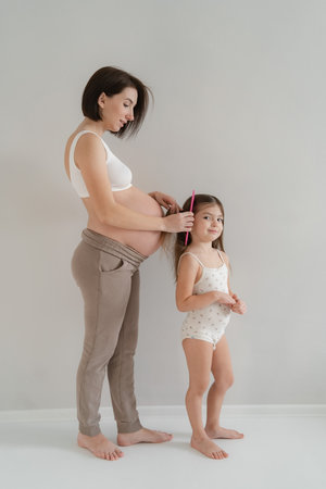 Young pregnant girl with a little daughter in a bright room in white home clothesの写真素材