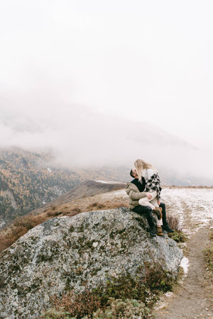 Bride and groom in a dress on a snowy road among the mountains in autumnの写真素材