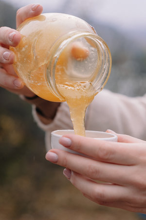Hands pour honey from a jar into a saucer