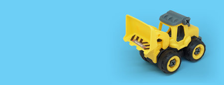 yellow plastic bulldozer toy isolated on blue background with copy space for toy store bannerの写真素材