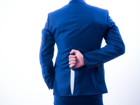 Young businessman holding knife on the back isolated from a white background.の写真素材