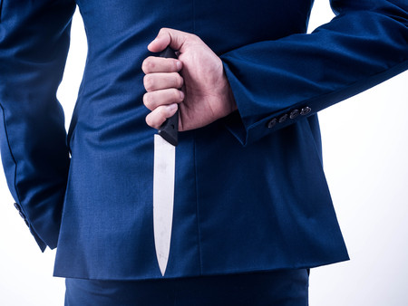 Young businessman holding knife on the back isolated from a white background.の写真素材