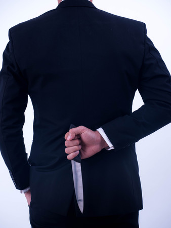 Young businessman holding knife on the back isolated from a white background.の写真素材