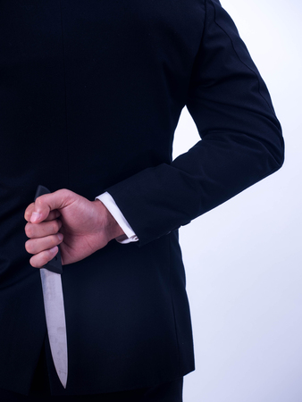 Young businessman holding knife on the back isolated from a white background.の写真素材