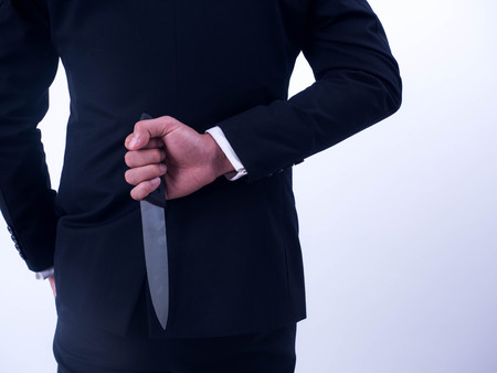 Young businessman holding knife on the back isolated from a white background.の写真素材