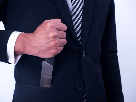 Young businessman holding knife in a suit pocket isolated from a white background.の写真素材