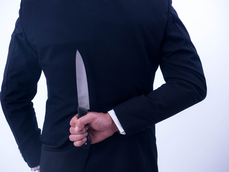 Young businessman holding knife on the back isolated from a white background.の写真素材