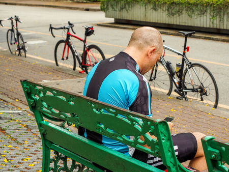 Cyclist taking a break, looking the mobile phone in he hand.のeditorial素材