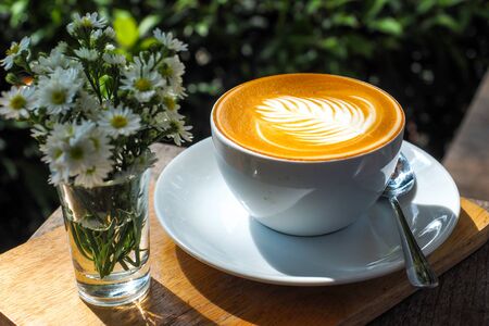 Coffee cup on a wooden table and the little flowers with light of the sun.の写真素材