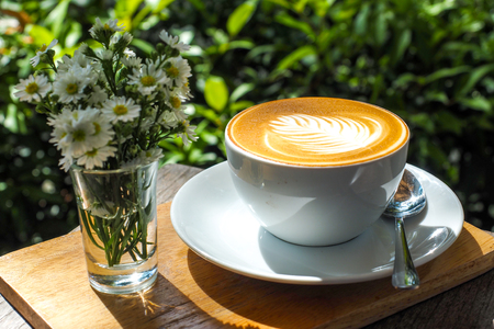Coffee cup on a wooden table and the little flowers with light of the sun.の写真素材