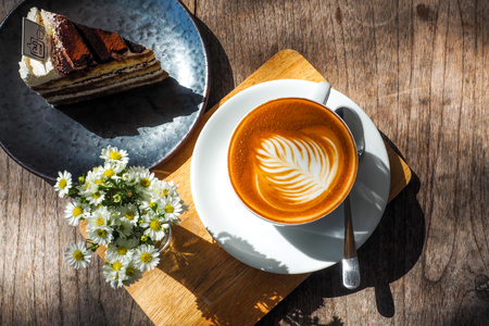 Coffee cup on a wooden table and the little flowers with cake.の写真素材