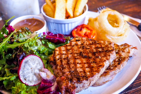 Grilled pork steak with vegetables salad and french friesの写真素材