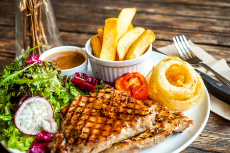 Grilled pork steak with vegetables salad and french friesの写真素材