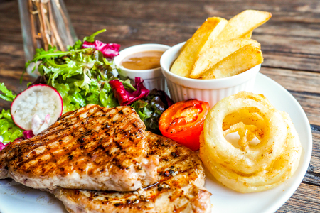 Grilled pork steak with vegetables salad and french friesの写真素材