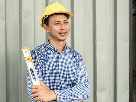 Portrait of an Engineer man holding level measuring instrument and standing at container box backgroundの写真素材
