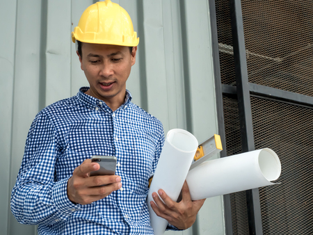 engineer hold blueprint paper construction drawing plan and holding mobile phone,Architect working in office,Engineering tools on desk at site projectの写真素材