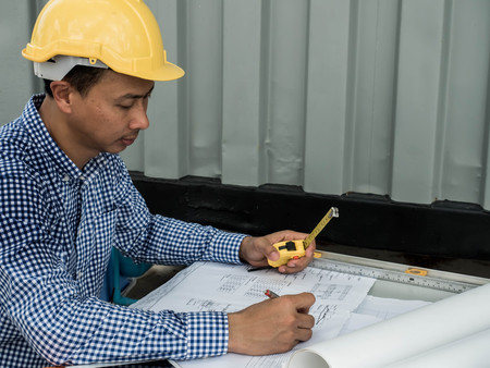 Engineer or Architect sitting working at his desk in the office checking on blueprint.の写真素材