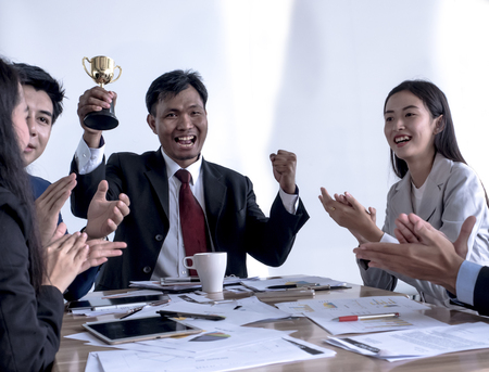 business man holding a gold trophy. Happy and successful business team rewarded for in the officeの写真素材