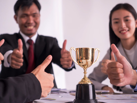 Businessman with teamwork in goal and successful showing trophy and thumb up rewarded for in the officeの写真素材