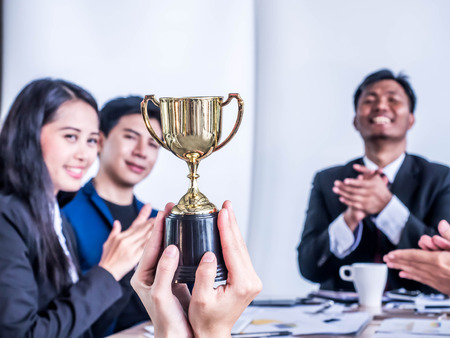 Businessman with teamwork in goal and successful showing trophy and rewarded for in the officeの写真素材