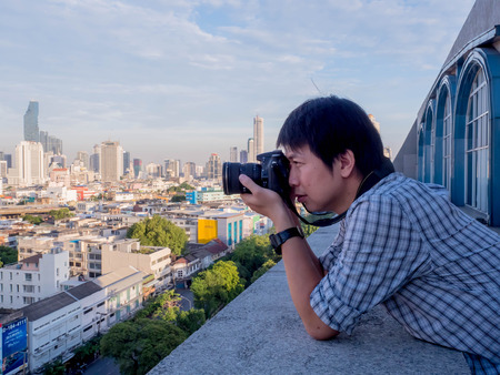 Young man shooting outdoor photos  take a picture of the city on a tall building.の写真素材