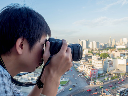 asian man , caucasian man standing and take a picture of the city on a tall building.の写真素材
