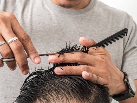 Attractive barber with dark hair doing a haircut for client with scissors isolated on white...