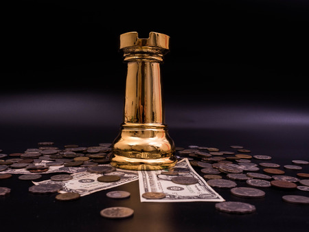 Chess leadership concept with gold on a pile of coins and banknotes isolated in black background....